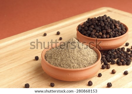 Black pepper powder and black pepper in terracotta pots on wooden plank