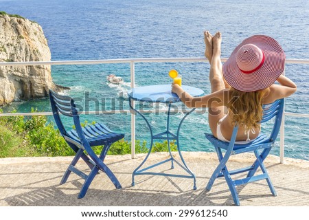 Young girl relaxing with drink and watching trip boats, Greek islands