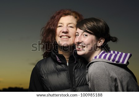 Two attractive women, one middle aged, one in her twenties, in affectionate embrace with twilight sky