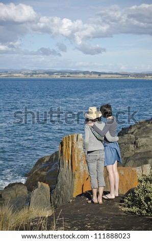 Mother and daughter linked arms by coastal rocks, Tasmania, Australia