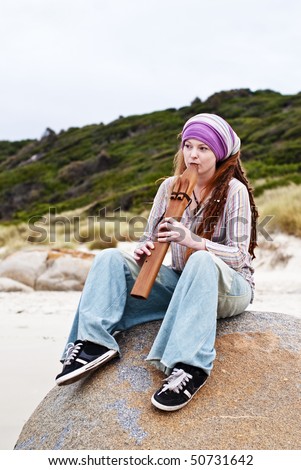 Beautiful young woman on rock playing native american pentatonic drone flute