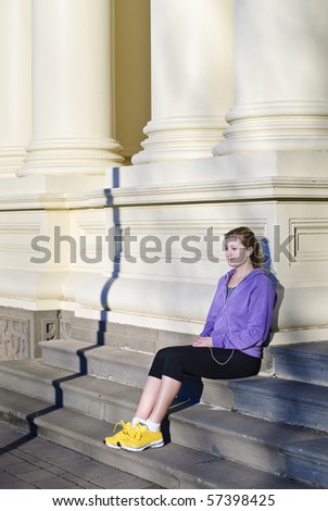 Woman wearing purple top and yellow sneakers listening to personal stereo on city steps