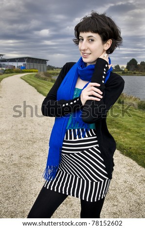Beautiful young woman with windblown hair wearing striped skirt and blue scarf in dynamic pose at vineyard