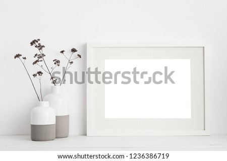 white frame mock up and dry twigs in vase on book shelf or desk. White colors.