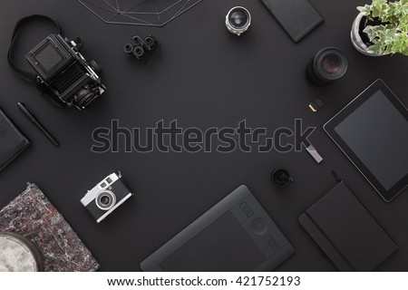 Work space on black table of a creative designer or photographer with laptop, tablet, cameras other objects of inspiration and copy space. Stylish home studio concept of technology trends.