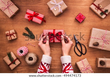 Woman wrapping modern christmas gifts. Close up on hands tying perfect bow. Wrapping inspiration. Christmas presents on a wooden table.