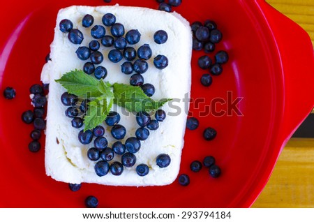 Fresh cottage cheese in a red bowl with a sprig of mint and blueberries on a wood