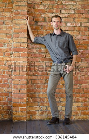Casually handsome. man standing against a wall of red brick and rests his hand on the wall. confident look