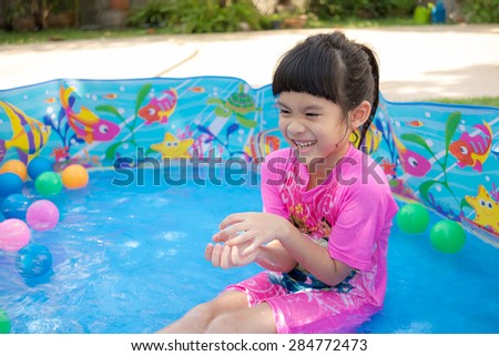 A baby girl in pink suit playing water and balls in blue kiddie pool