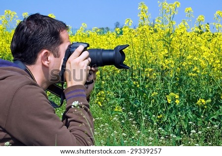 Young male photographer taking photos of yellow flower field