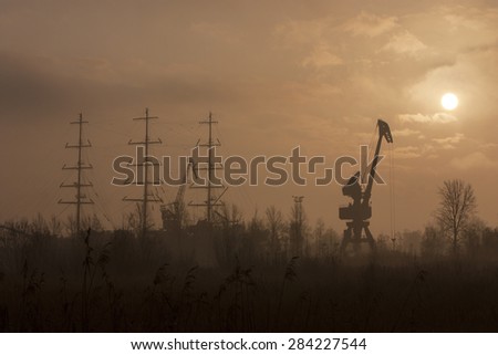silhouette of port with the crane and the ship at sunset among trees