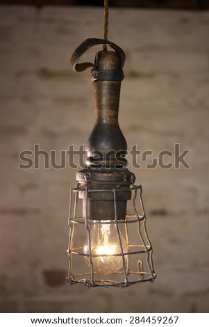 Vintage caged inspection lamp/contemporary style interior light, featuring metal cage, glass dome, wooden handle and leather hanging strap. White painted industrial brick wall background