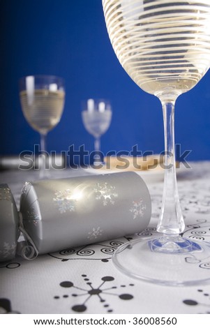 Close up of Christmas crackers, glasses of wine and mince pies on a dining table with blue wall background.