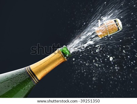 Bottle of Champagne with popping cork and Champagne spray on black background.