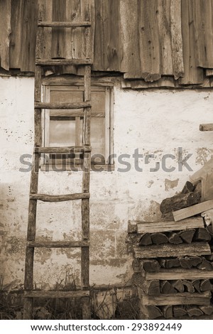 Old wooden ladder on wooden wall over window under slate roof, vintage effect