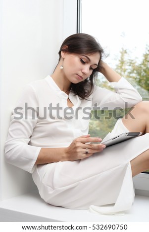 Young pretty woman sitting at  window reading a tablet PC enjoys of rest
