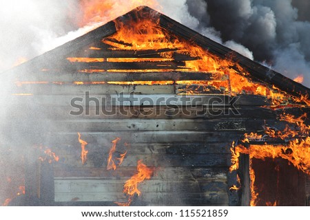 A blazing fire burns through the roof rafters of an old farm home.