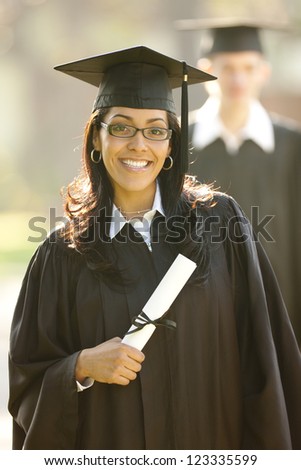 Outdoor portrait of a Hispanic female graduate wearing a graduation cap and gown holding her diploma
