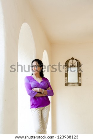 Latin woman looking away from camera leaning next to arches with mirror on the wall