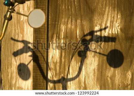 Shadow of bicycle handlebars, with mirrors, on peeling wood background