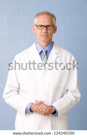Medical professional in lab coat wearing glasses on blue background three quarter length, looking to camera