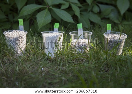 In the bright sunbeams fertilizer in plastic cups surrounded by bright green grass. On the stickers is recorded of fertilizer formula.