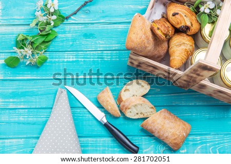 Slices of bread and a knife lying on a turquoise wooden table with a napkin and a sprig of apple/Sliced bread and other baked in a wooden box on a turquoise table.