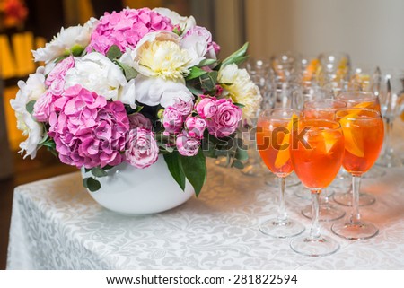 Glasses with an exotic cocktail and orange slices on a table next to a bouquet of flowers/Orange exotic cocktail served at the table with a bouquet of flowers.