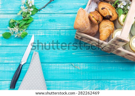 Turquoise wooden table served with a knife, cloth and wooden box of pastries./Wooden box with cakes on a wooden table.
