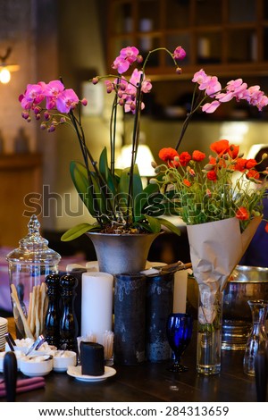 Orchid flowers in a decorative vase on a wooden table with candles and cutlery/Flowers on the table in a restaurant