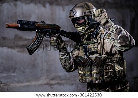 Armed ranger in camouflage,mask and helmet shows special signal during a special military operation in the building/Armed ranger in camouflage,mask and helmet shows special signal