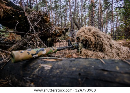 Sniper in camouflage suit is hiding and aiming behind a tree/Camouflaged sniper lying in forest and aiming through his scope