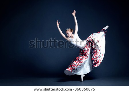 Young ballerina with a perfect body is dancing in the photo studio. The dancer wears a fashionable dress. The photo is taken in minimal style, showing the beauty of a such classical art like ballet.