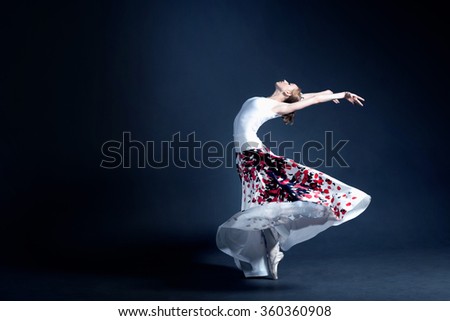 Young ballerina with a perfect body is dancing in the photo studio. The dancer wears a fashionable dress. The photo is taken in minimal style, showing the beauty of a such classical art like ballet.