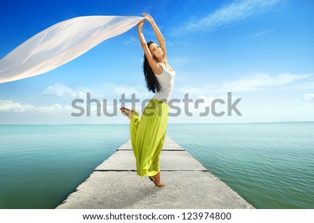 Joyful young woman jumping with white tissue against seascape