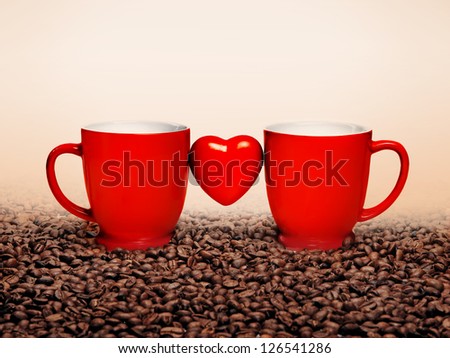 Two red coffee cups and shape of heart on brown background of coffee beans