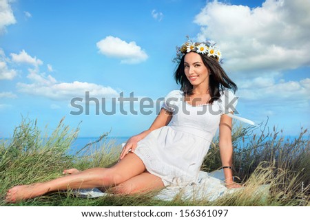 Beautiful smiling brunette in white dress and  flower wreath on head against blue sky