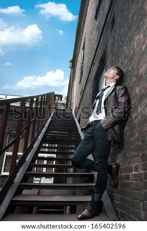 Portrait of dreamy stylish guy standing near old brick wall