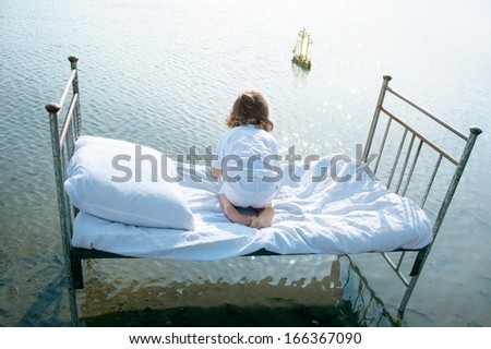 Dreamy child on vintage bed in sea look at toy sailboat. Summer romantic concept