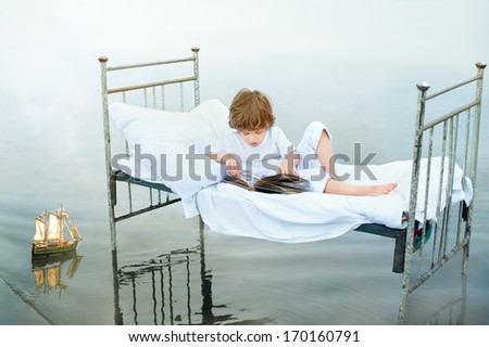 Child looking at old album on vintage bed in water on sea shore