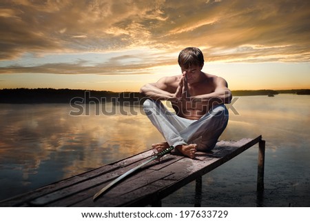 Portrait of young warrior with Japanese sword on sunset background Portrait of young warrior with Japanese sword on sunset background