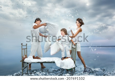 Happy young family fight a battle by pillows on a bed in the sea