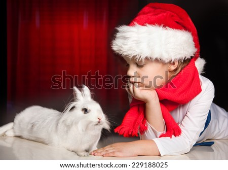 Dreamy boy in New Year hat with white rabbit on dark red background