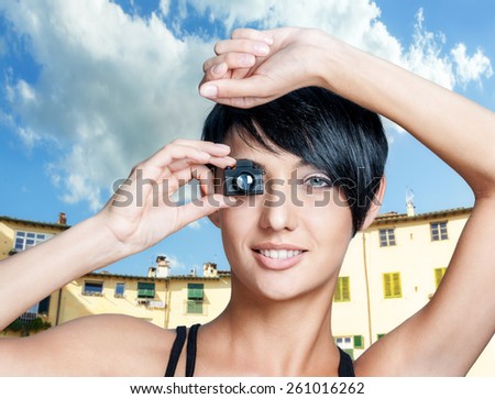 Portrait of beautiful smiling woman with toy small camera against urban outdoor background