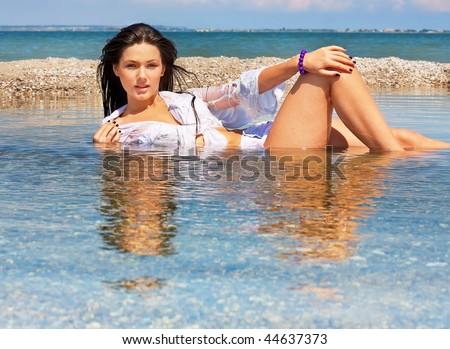The beautiful young girl in wet clothes lies in water on seacoast