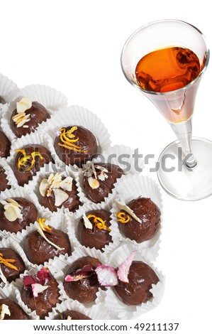 Chocolate truffles in a paper wrapper and liquor in a wine-glass on a white background