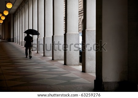 Urban scene of architectural colonnade and silhouette of person with umbrella. Stockholm