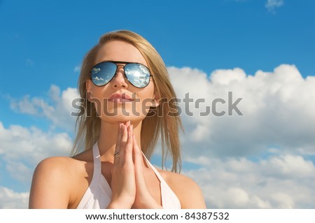 Meditation of young woman in mirrored sunglasses against blue sky