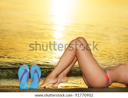 Female legs and blue sandshoes against of sea sunset