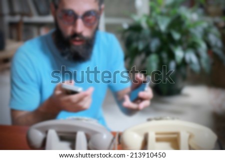 Bearded man with glasses, smartphone and old phones, intentionally blurred background